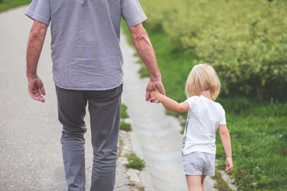 Дедушка за руку с маленькой внучкой на прогулке